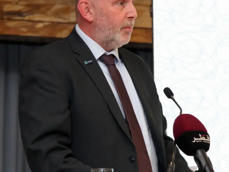A speaker addressing the hall from the lectern, 2025.