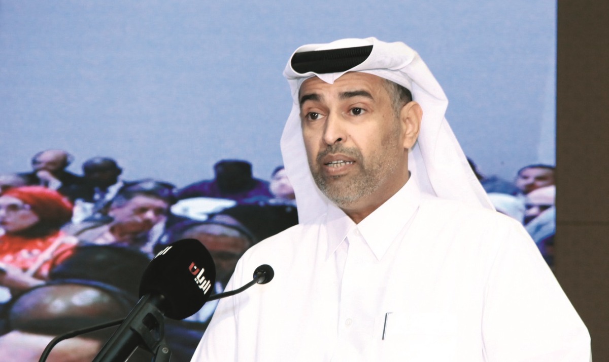 A Qatari official speaking at the lectern during the inaugural ESG Qatar conference in 2024, with a live feed of the seated audience on the screen behind him.